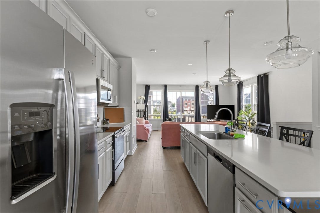Galley-style kitchen featuring stainless steel appliances, white cabinetry with hardware accents, quartz countertops, and pendant lighting