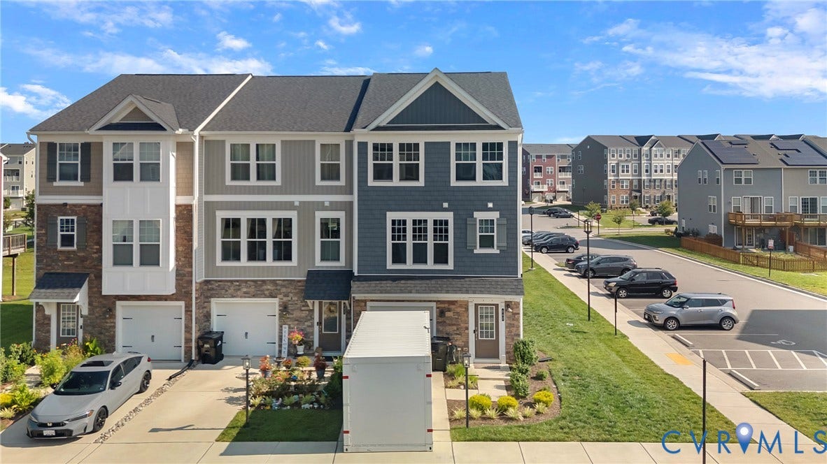 Multi-level townhome with an attached garage, paved driveway, and stone veneer accents
