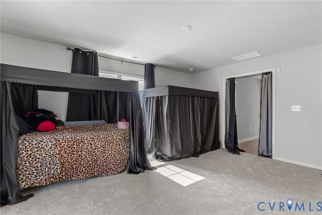 Spacious primary bedroom suite featuring carpet flooring, high ceilings with recessed lighting, and a four-poster canopy bed frame with blackout drapery