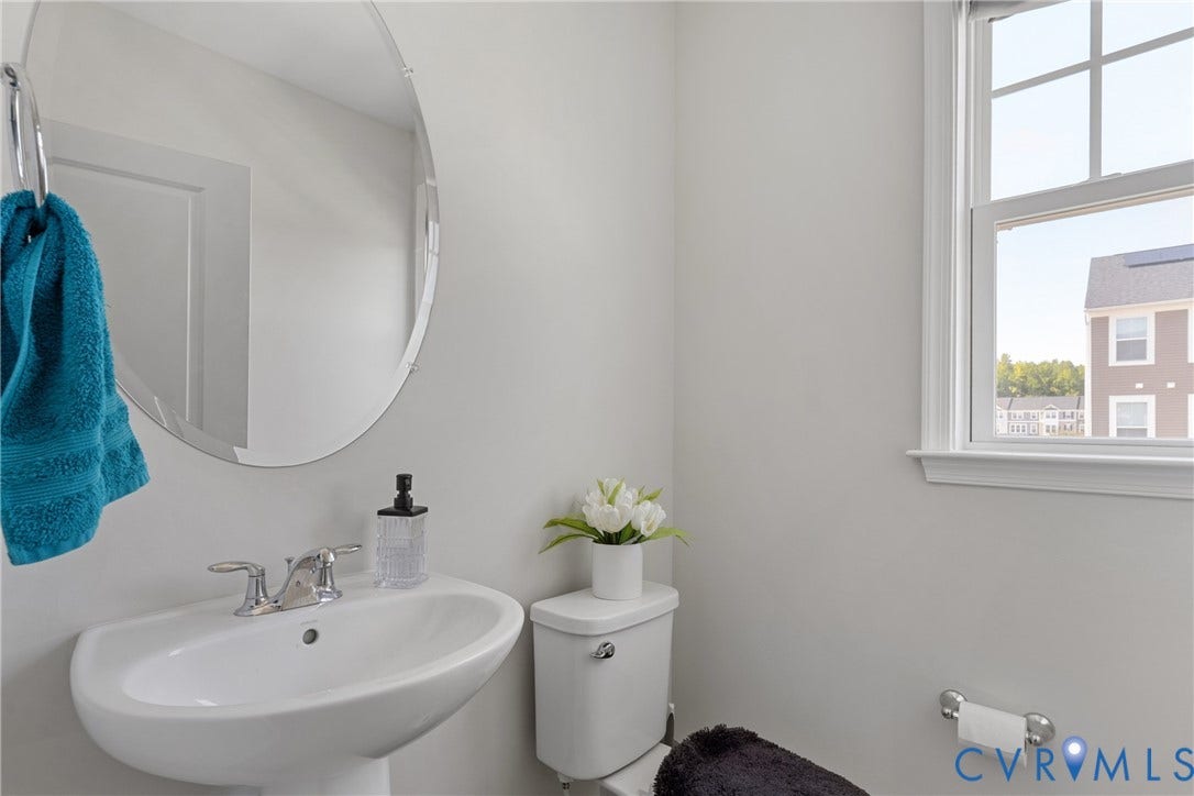 Bright bathroom featuring a curved vanity sink with chrome faucet and fixtures, large circular mirror, white cabinetry, and abundant natural light from a multi-pane window