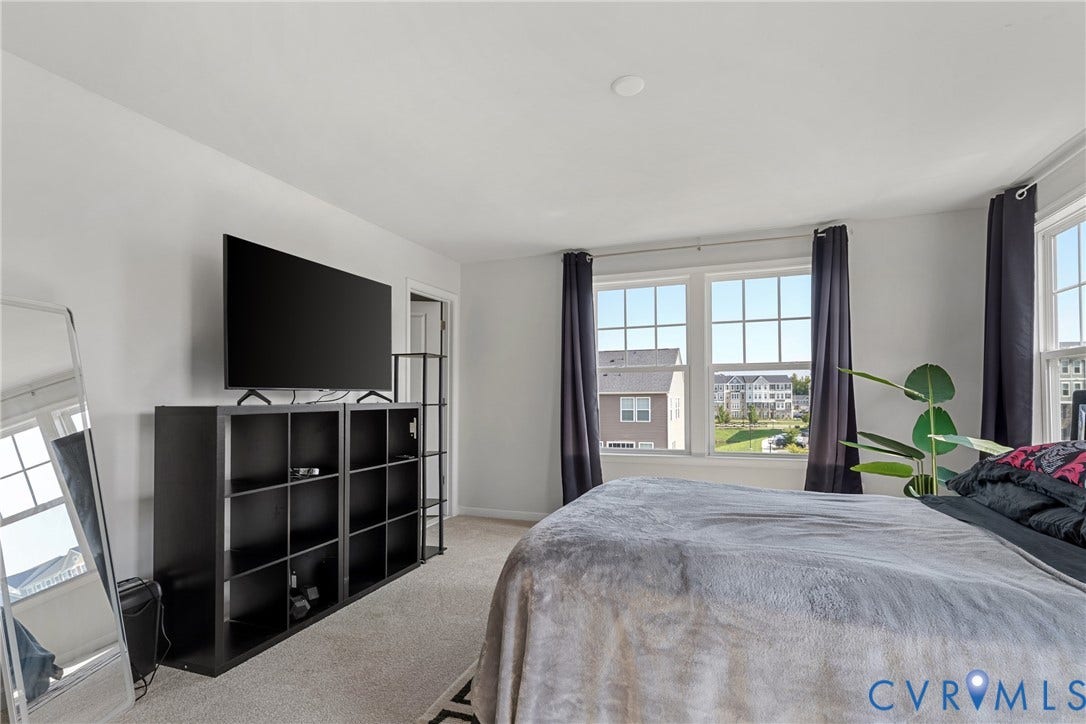 Spacious primary bedroom featuring abundant natural light from expansive multi-pane windows, neutral carpeting, and a large black storage shelving unit