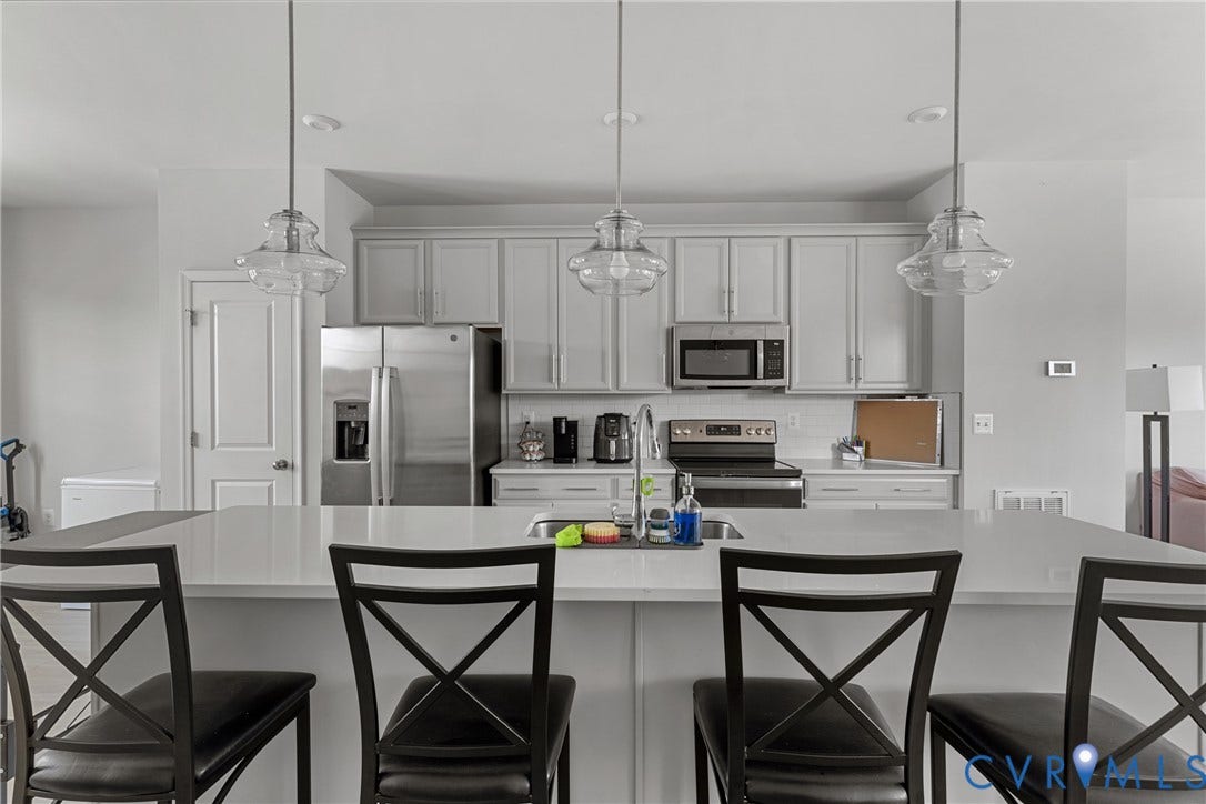 Chef's kitchen featuring custom cabinetry with paneled doors, stainless steel appliances including a French-door refrigerator and built-in microwave, and pendant lighting above a waterfall-edge island