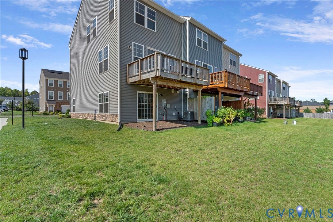 Spacious rear elevation featuring a three-story gray vinyl siding exterior with multiple windows, a two-tiered wooden deck with metal railings, and an open-air covered patio beneath