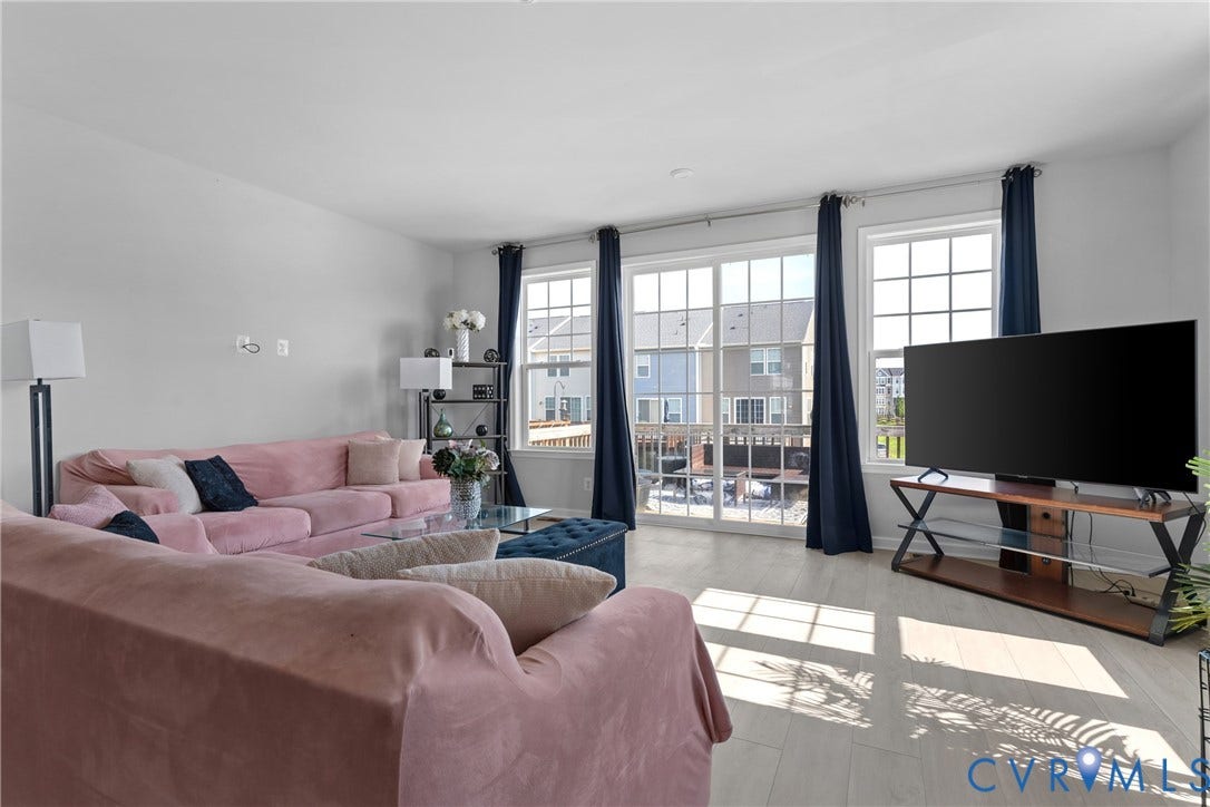 Bright, sun-filled living area showcasing expansive glass doors and windows, light wood-finish flooring, and high ceilings