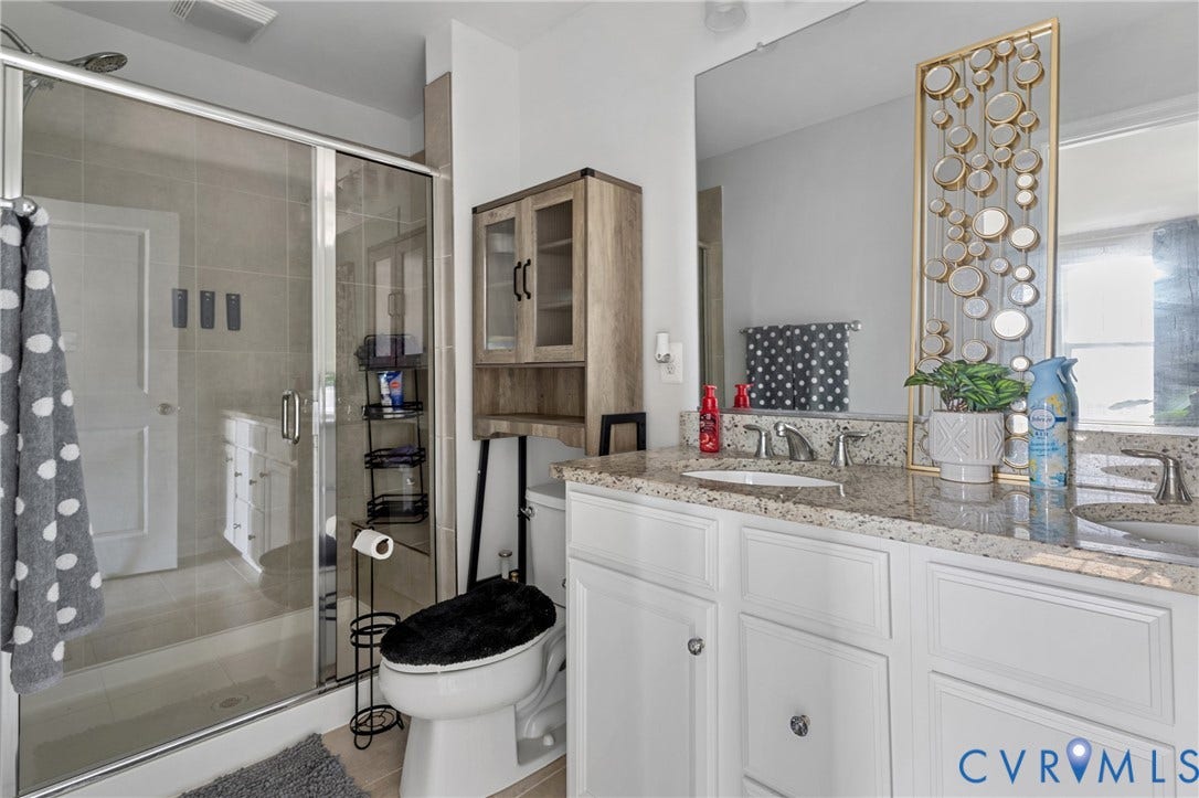 Spa-inspired primary bathroom featuring dual vanities with white cabinetry, granite countertops, and chrome hardware