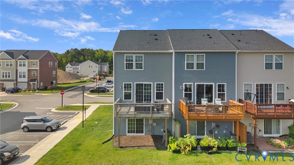 Modern two-story residence featuring a composite deck with integrated seating areas, expansive manicured lawn, and multiple French doors providing natural light to the lower level