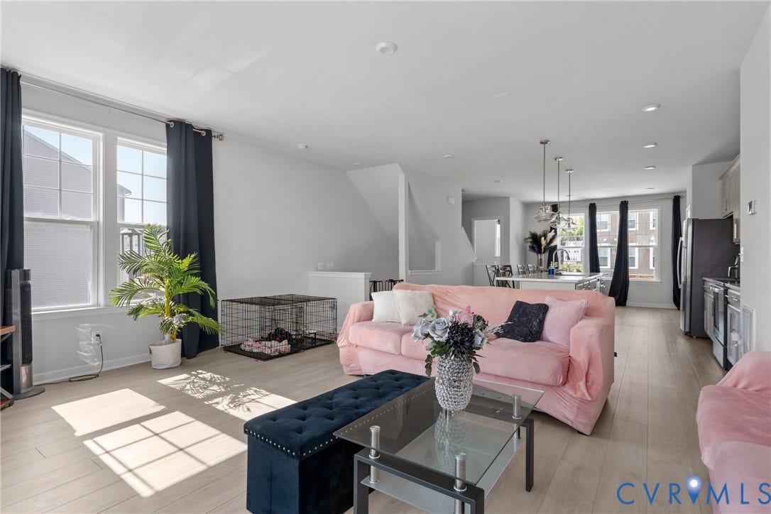 Bright, open-concept living area showcasing light wood-finish flooring, expansive windows with natural light, recessed ceiling lighting, and a gas fireplace