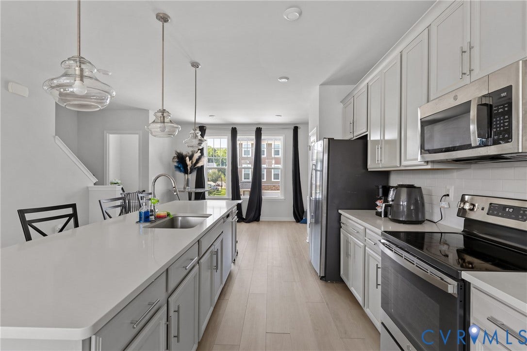 Modern kitchen featuring light gray cabinetry, stainless steel appliances, a large island with an undermount sink, and wood-finish flooring