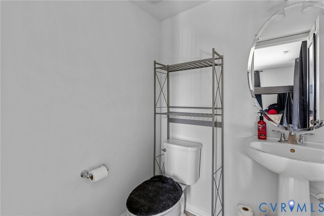 Compact bathroom featuring a pedestal sink with integrated countertop, large arched mirror with integrated lighting, and metal shelving unit positioned above the toilet for efficient storage