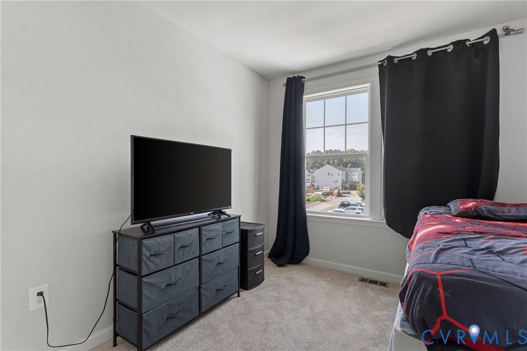Bright bedroom featuring large window with natural light, carpeted flooring, and built-in storage dresser with multiple drawers