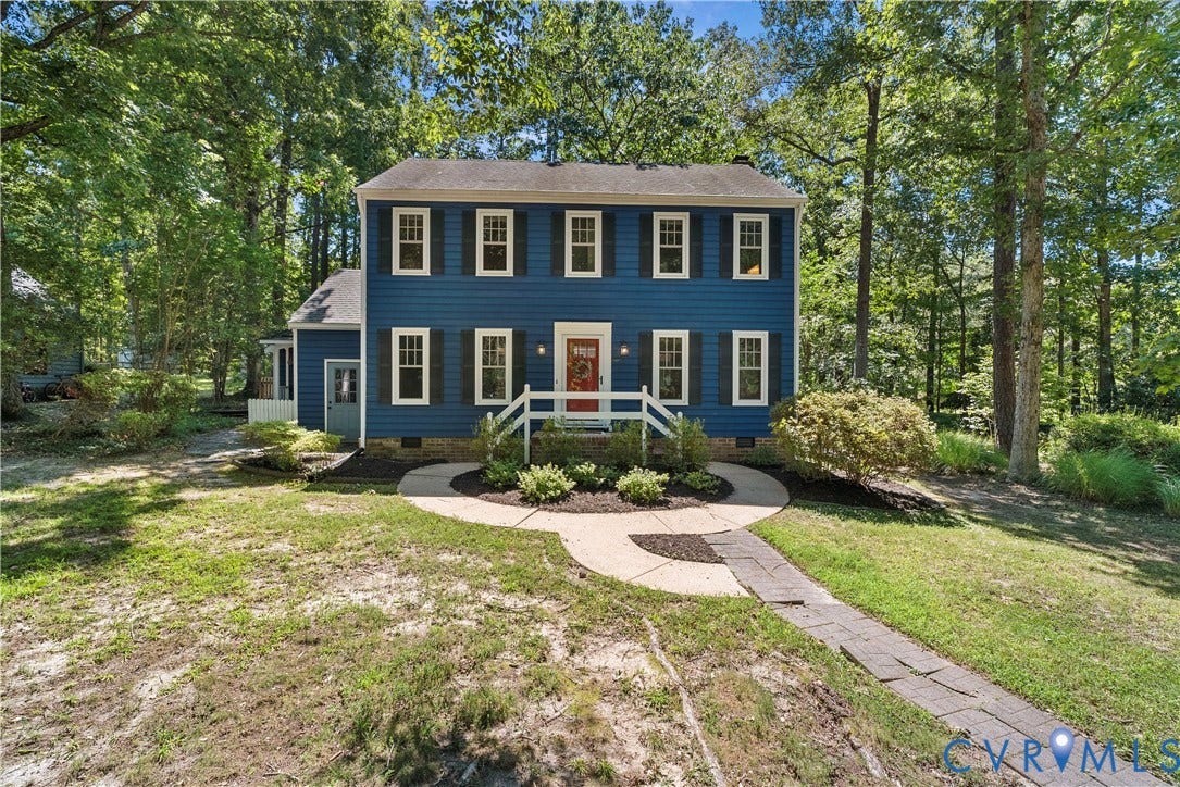 Colonial-style residence featuring a deep blue exterior with cream-trimmed windows, brick chimney, and a welcoming front entrance with a covered porch and brick walkway