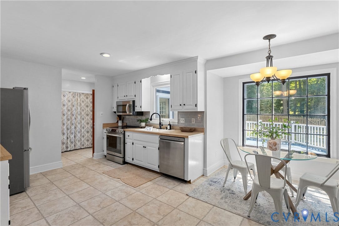 Bright, open kitchen and dining area featuring stainless steel appliances, white cabinetry with wood-finish countertops, tile flooring, recessed and pendant lighting, and French doors with multiple panes opening to an outdoor deck with metal railings