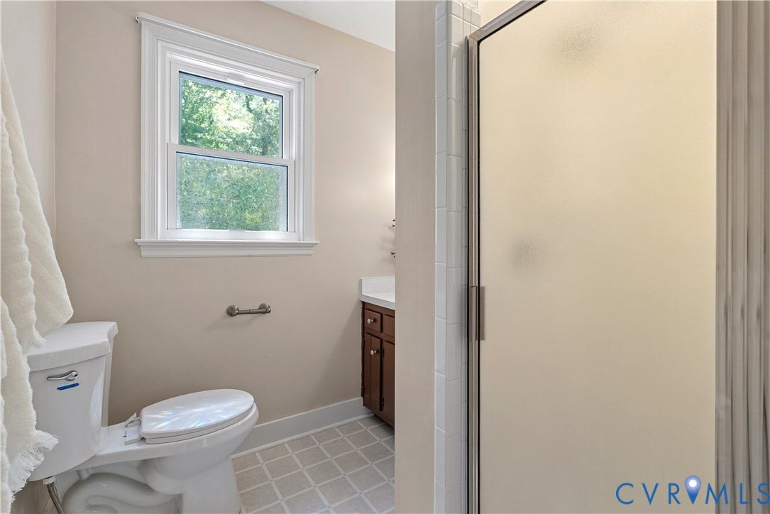 Bright, updated bathroom featuring a white porcelain toilet, tile flooring, and a large walk-in shower enclosure with frosted glass doors