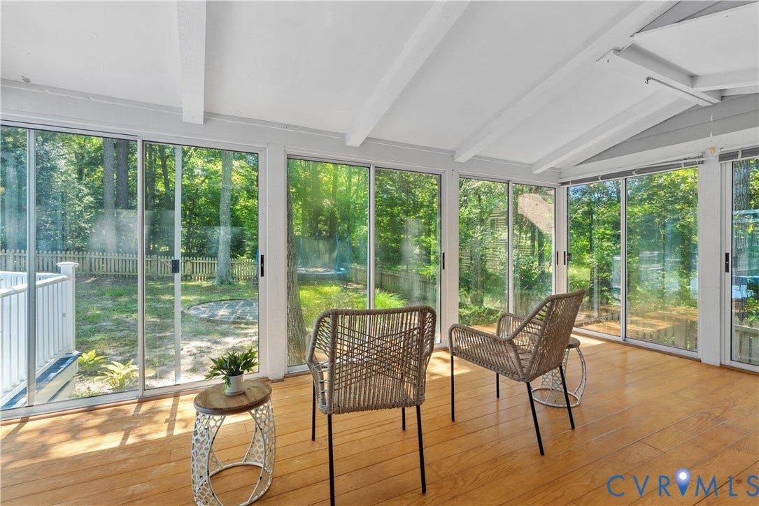 Sunlit sunroom with expansive glass wall systems offering panoramic vistas of mature landscaping and grounds