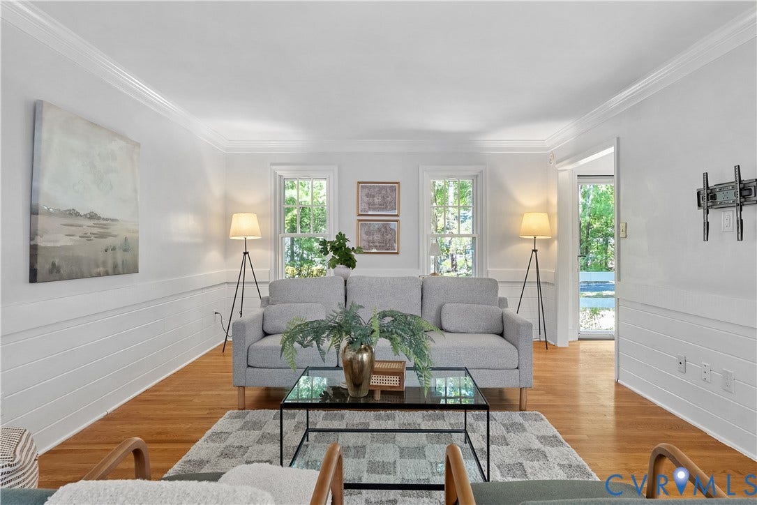 Bright living room featuring hardwood flooring, white shiplap walling with chair rail detailing, and multiple tall windows with natural light