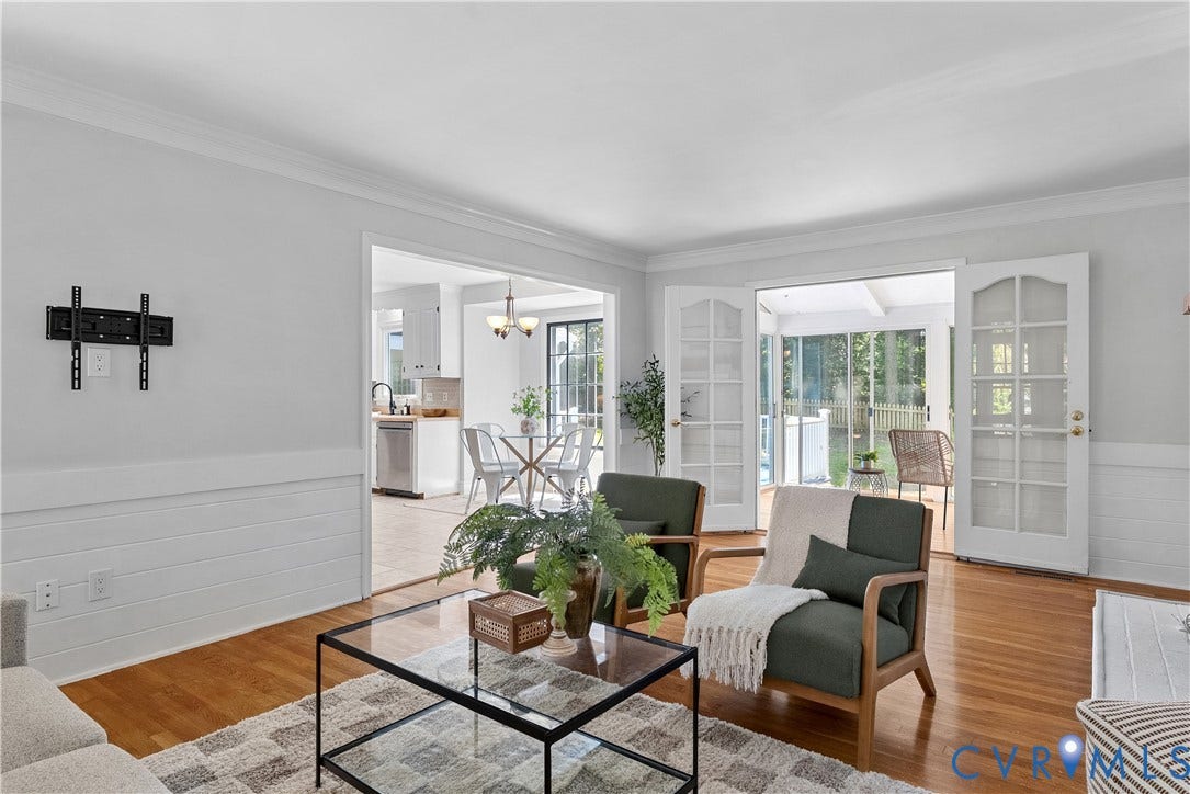 Bright living room with hardwood flooring, wainscoting detail, and large glass French doors opening to outdoor space