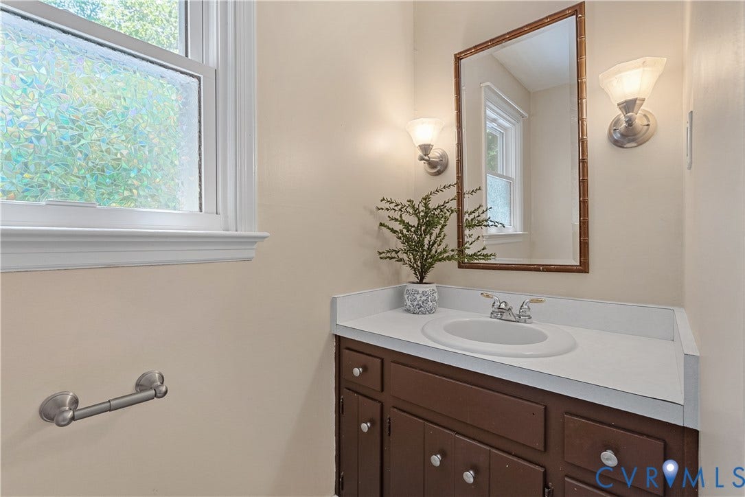 Elegant bathroom featuring a wood-finish vanity with multiple drawers and brushed nickel hardware, white marble-look countertop, and an oval undermount sink