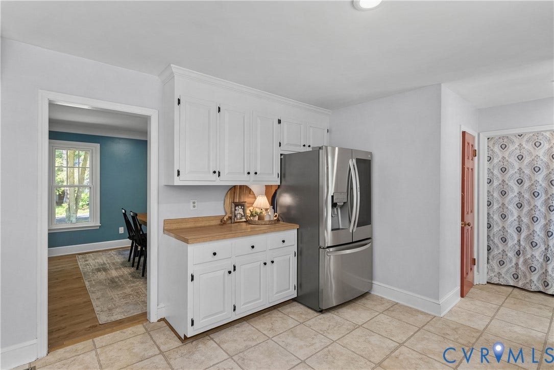 Bright kitchen featuring white cabinetry with black hardware, wood-finish countertops, and stainless steel French-door refrigerator with ice and water dispensers