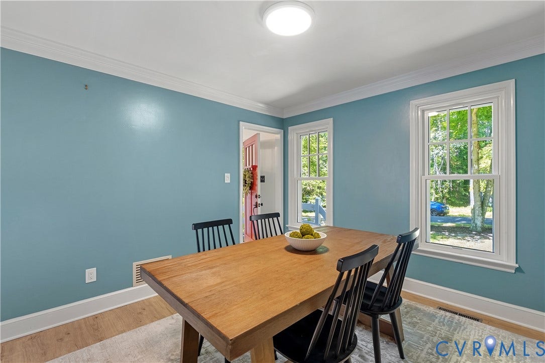 Bright dining room showcasing soft blue walls, hardwood flooring, and abundant natural light from oversized windows