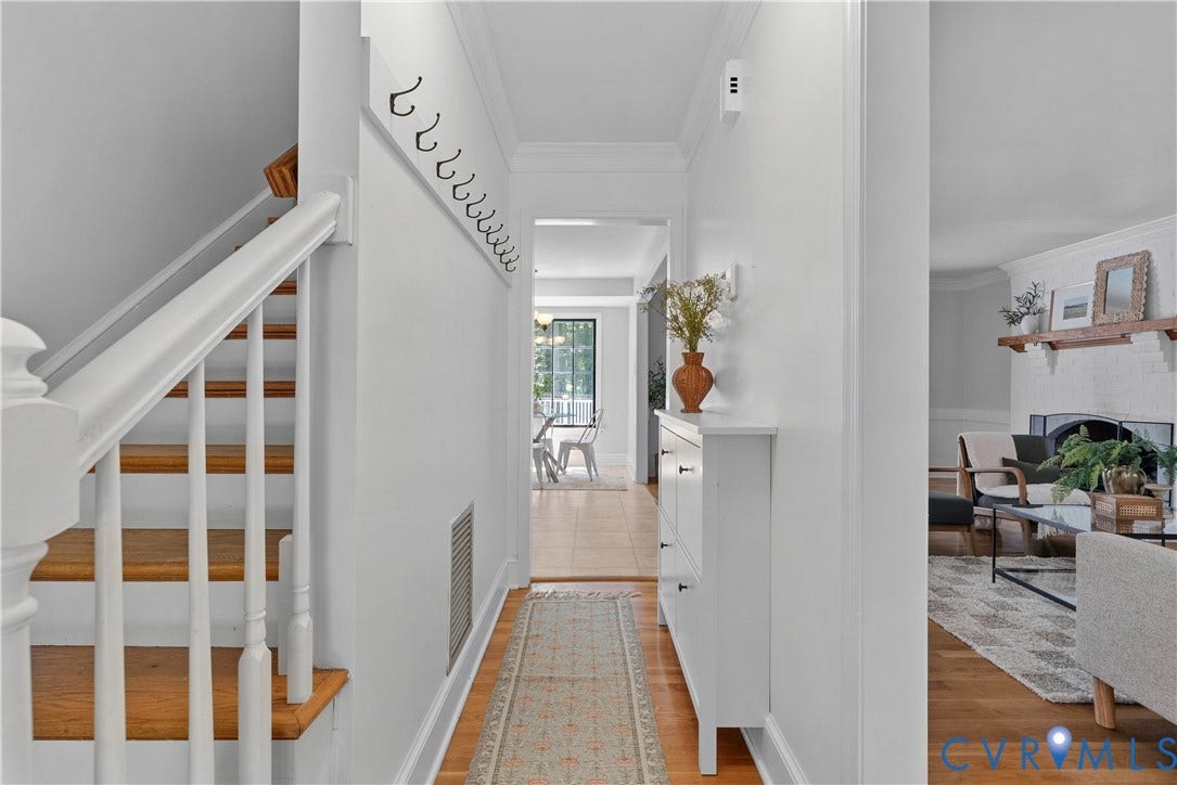 Bright hallway flooded with natural light through expansive windows, featuring hardwood flooring, white painted walls, and a curved staircase with wood treads and white railings
