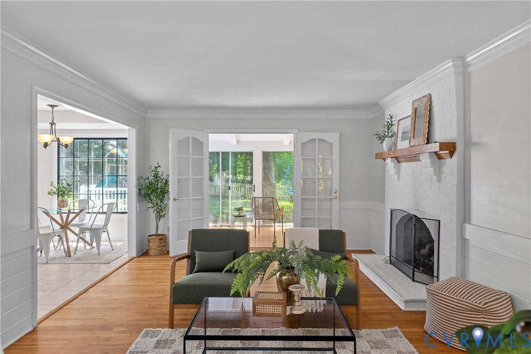 Bright, light-filled living room featuring hardwood flooring, a fireplace with built-in surround, and abundant natural light from French doors leading to an adjoining sunroom