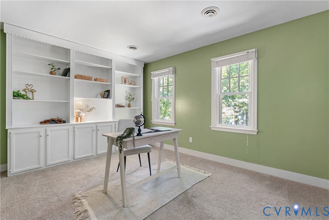 Sophisticated home office featuring sage green walls, abundant natural light from dual casement windows, and extensive built-in cabinetry with open shelving and lower storage