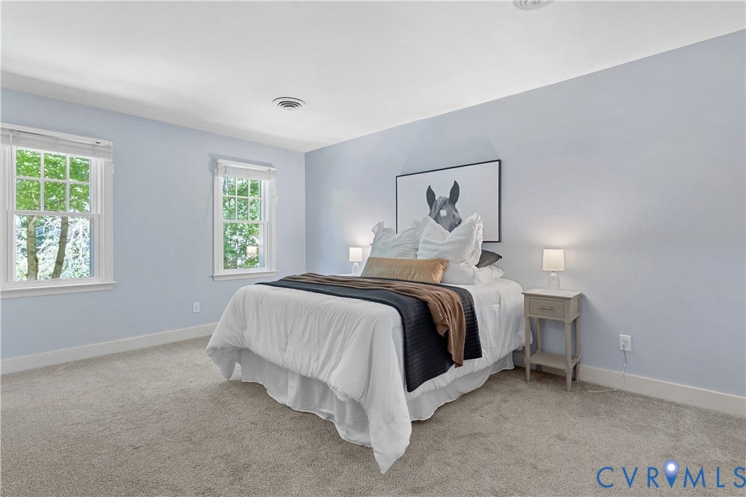Serene primary bedroom showcasing soft periwinkle walls, abundant natural light from dual casement windows, neutral carpeting, and paired bedside tables with integrated lighting