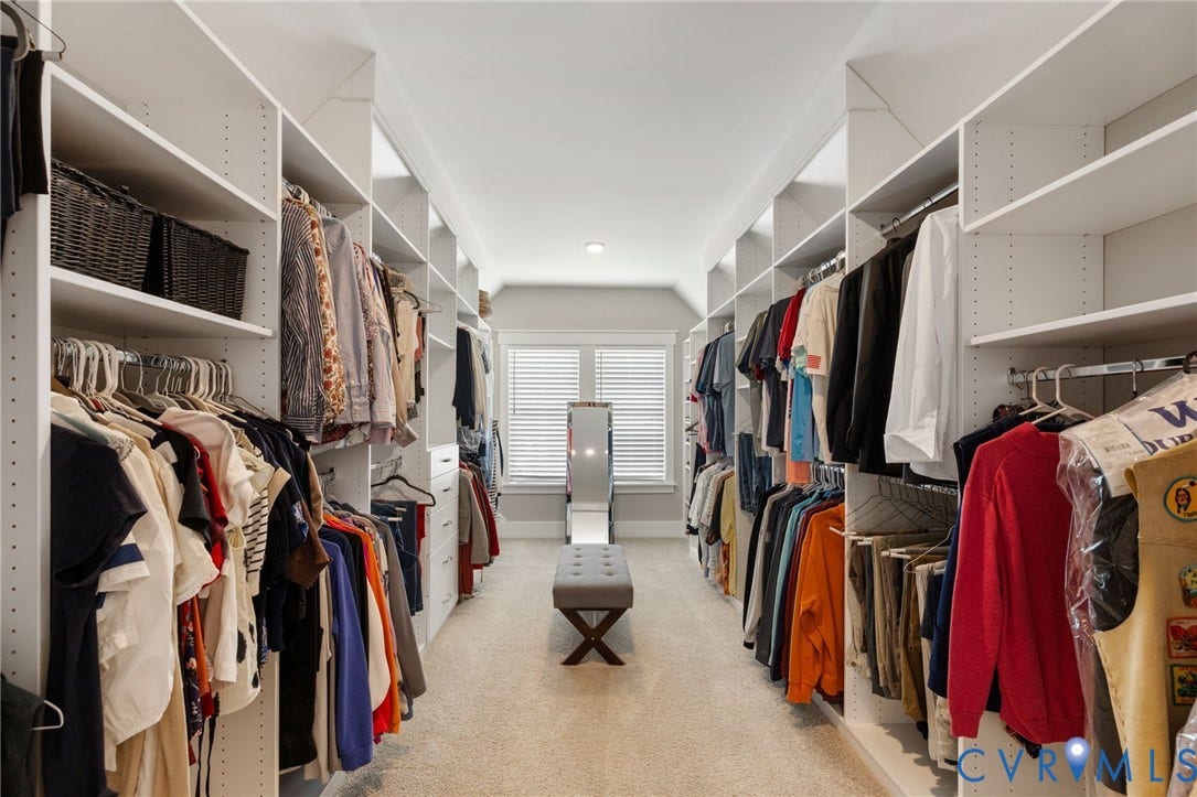 7237 Bonallack Bend, Carlton Ridge, Moseley, VA 23120 Spacious walk-in closet featuring extensive built-in shelving and hanging rods along both walls, neutral carpeting, and natural light from a central window with plantation shutters