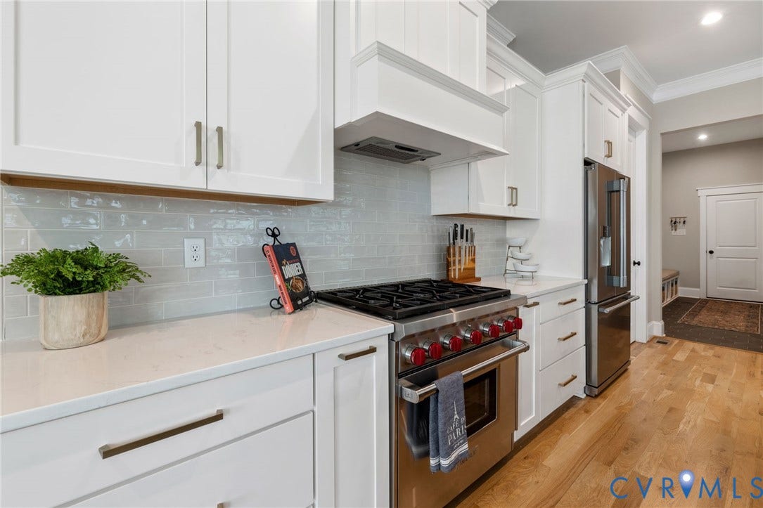 7237 Bonallack Bend, Carlton Ridge, Moseley, VA 23120 Chef's kitchen with Wolf 6 burner gas range, tons of quartz countertops, extensive white cabinetry, large center island with counter seating, stainless steel appliances, walk-in pantry, backsplash, and pendant lighting