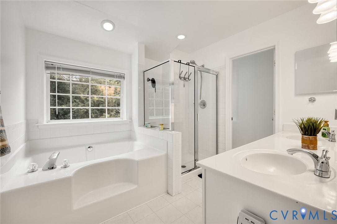 10620 Correnty Drive, Henrico, VA 23059 Bright bathroom featuring a built-in tub, separate glass-enclosed shower, dual vanity with undermount sinks, and a large window with privacy blinds