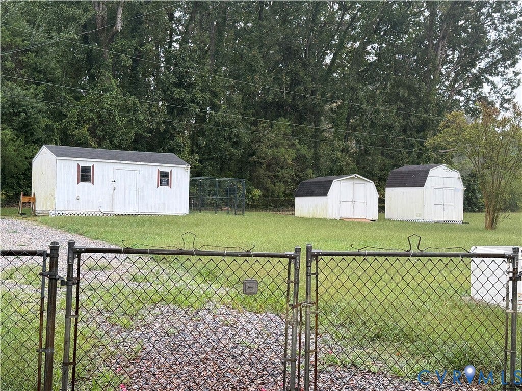 11925 Wedge Drive, Chester, VA 23831 Chain link fence with gate, gravel driveway, three storage sheds, and a grassy area