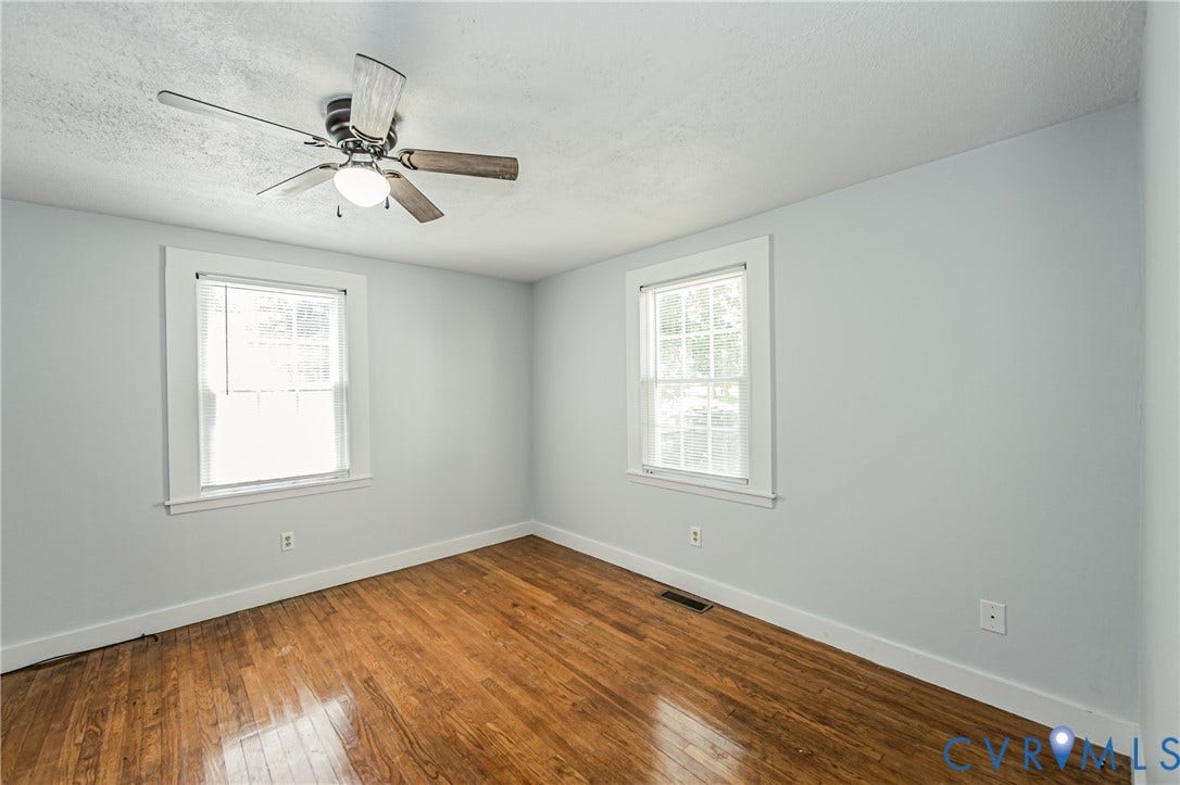Bedroom featuring wood-finish flooring, two large windows with white trim, and a ceiling fan with integrated lighting