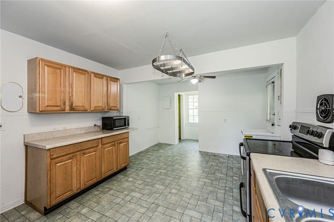 Kitchen featuring wood cabinetry, laminate countertops, a stainless steel sink, patterned tile flooring, and a ceiling fan with integrated lighting