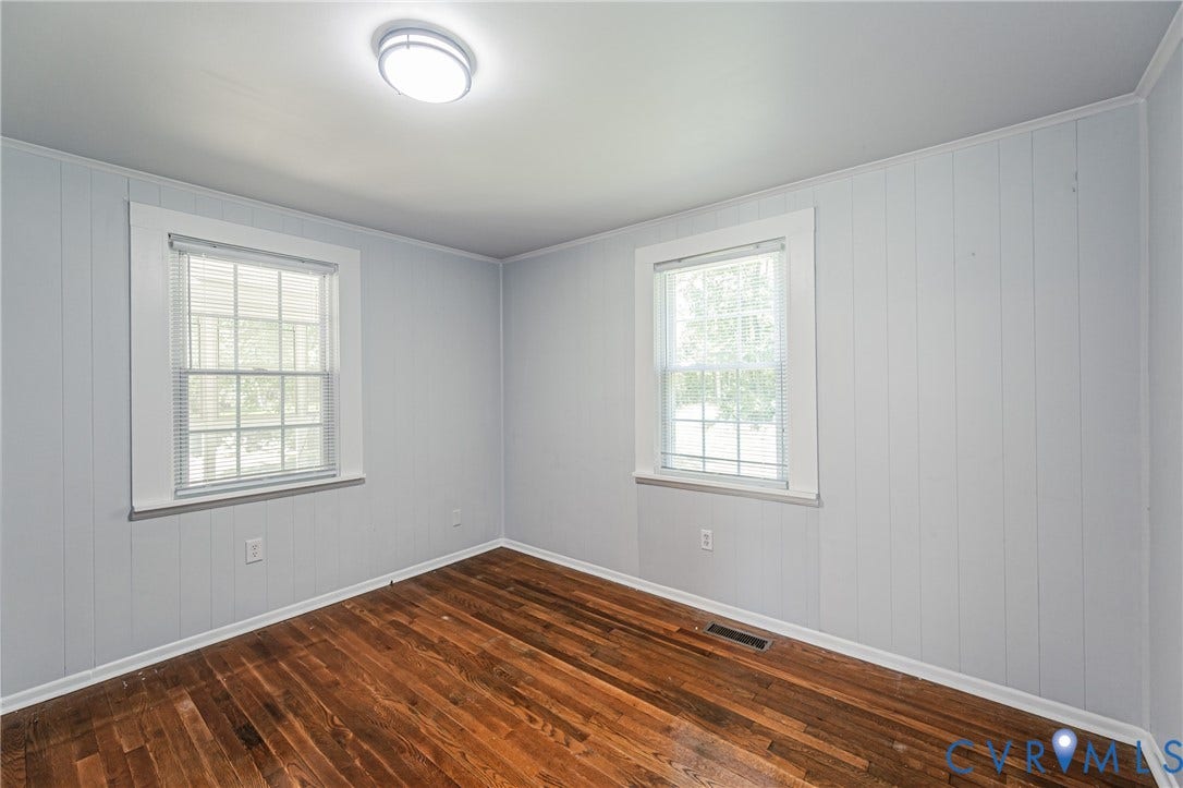 Hardwood flooring throughout, featuring two windows with horizontal blinds, and a ceiling-mounted light fixture