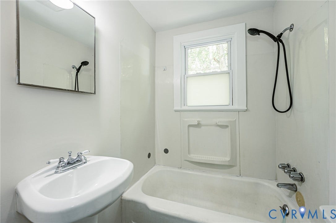 Bathroom featuring a pedestal sink, framed mirror, and a bathtub with an integrated shower fixture