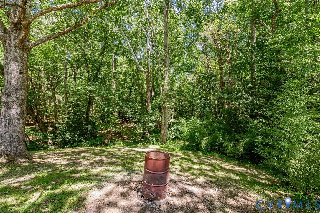 Expansive outdoor space featuring a fire pit on a gravel base, surrounded by a lush, verdant treeline