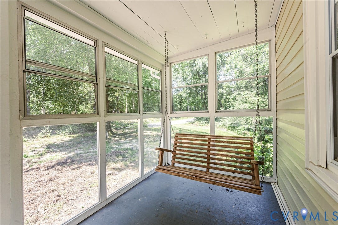 Screened porch featuring a wooden porch swing, multiple large windows, a painted concrete floor, and horizontal siding on the exterior wall