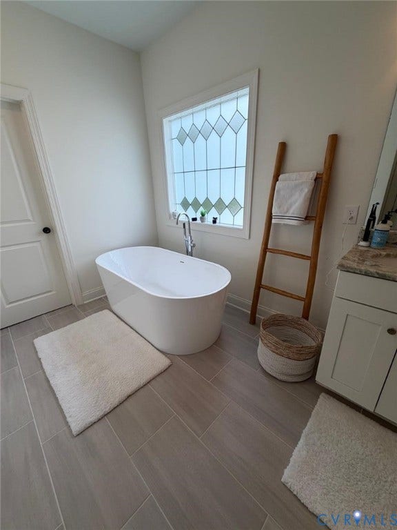 4516 Bacova Club Court, Glen Allen, VA 23059 Freestanding tub with a floor-mounted faucet, patterned privacy window, tile flooring, and a single vanity with a stone-finish countertop