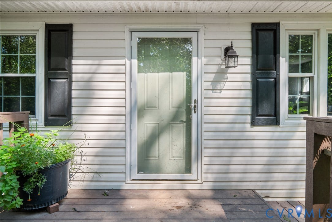 3940 Three Bridge Road, Powhatan, VA 23139 Light-colored horizontal siding, dark window shutters, clear storm door, wooden deck flooring, and an exterior wall lantern