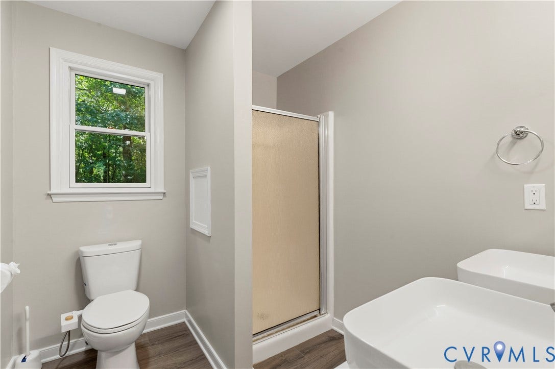 9007 Chatham Grove Lane, Richmond, VA 23236 Primary ensuite bathroom - White-framed window, wood-finish flooring, standing shower with frosted glass, dual rectangular vessel sinks, and a chrome towel ring