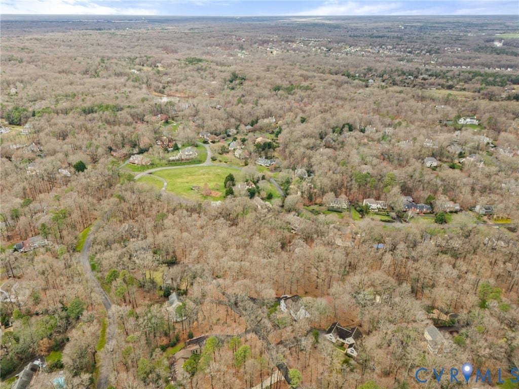Aerial view showcasing an expansive wooded property with mature trees, rolling terrain, and multiple structures nestled throughout the landscape