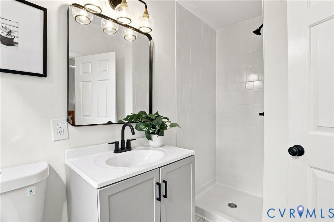 625 N 33rd Street, Chimborazo, Richmond, VA 23223 Modern bathroom featuring a single vanity with a white countertop and dark hardware, a framed mirror, and a tiled walk-in shower with dark fixtures