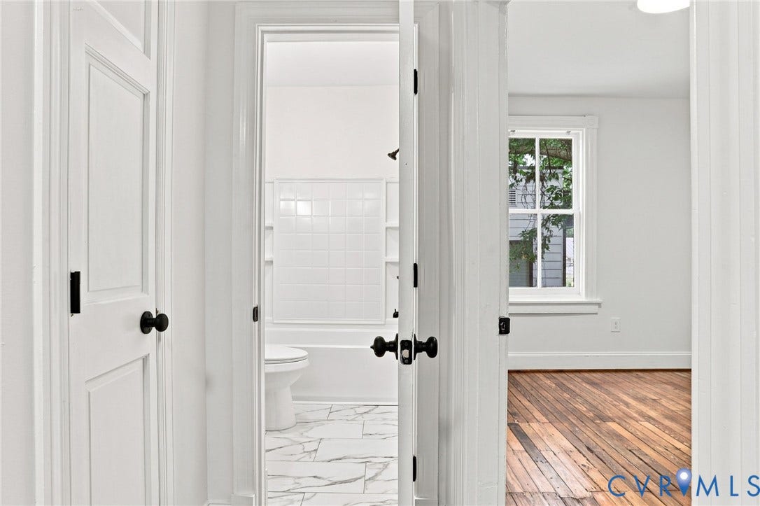 625 N 33rd Street, Chimborazo, Richmond, VA 23223 White panel doors with matte black hardware, white tiled shower surround, marble-finish floor tiling, wood-finish flooring, and white trim window
