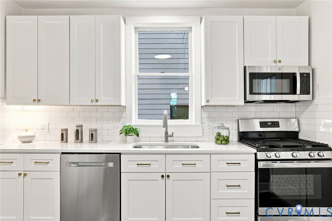 625 N 33rd Street, Chimborazo, Richmond, VA 23223 Contemporary white cabinetry with brushed brass hardware frames this kitchen, featuring stainless steel appliances including a gas range, built-in microwave, and dishwasher