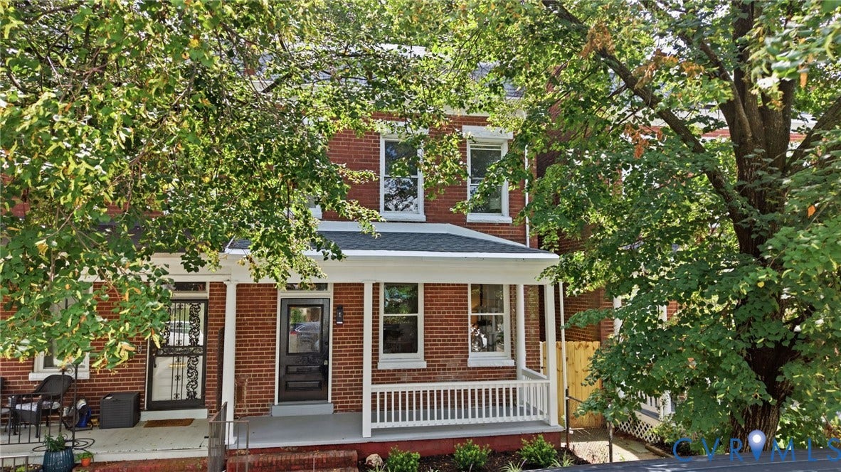 625 N 33rd Street, Chimborazo, Richmond, VA 23223 Classic brick Colonial with welcoming front porch featuring white railings and columns, mature shade trees framing the property, and charming architectural details including upper-level dormers and multi-pane windows