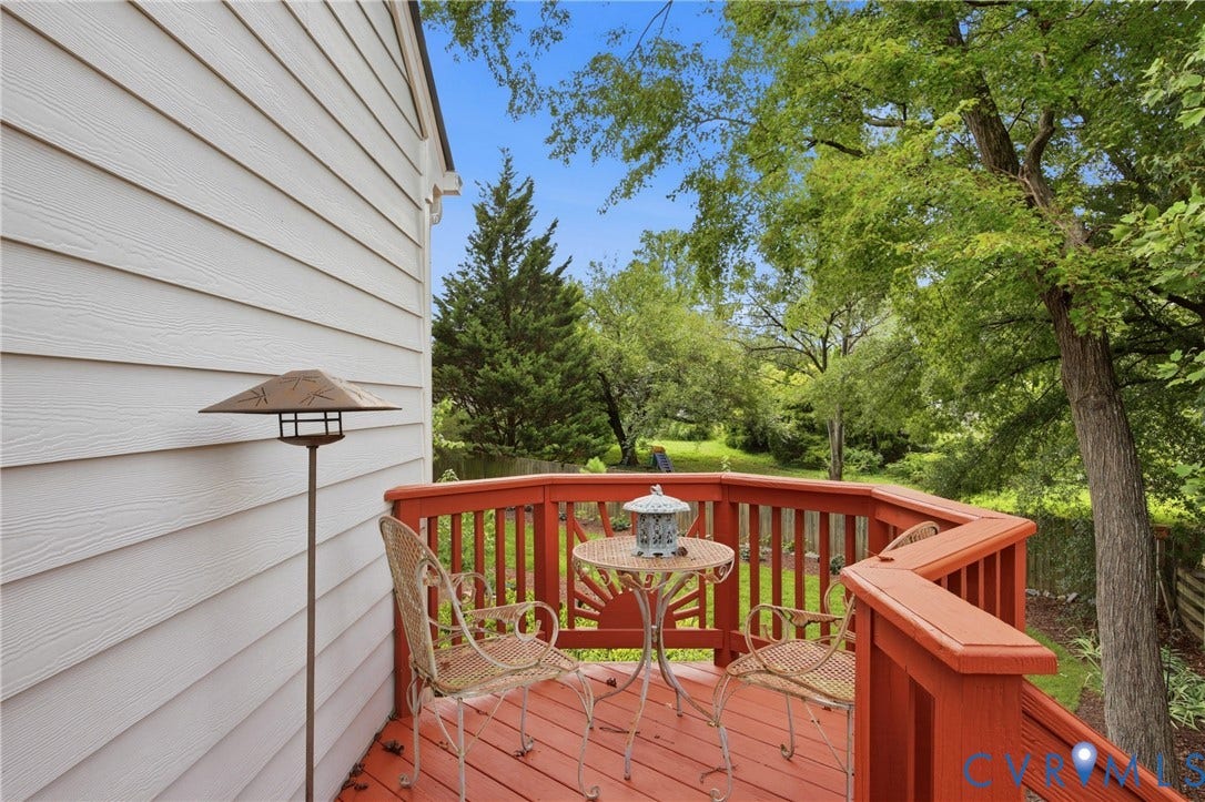 Expansive composite deck featuring rich wood-finish railings and multiple entertaining zones, overlooking mature landscaping with established trees and natural woodland backdrop