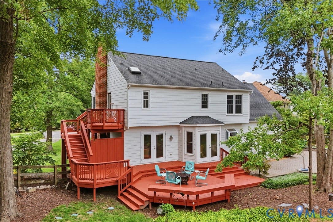Multi-level outdoor deck featuring a brick chimney, white siding, multiple windows, and a bay window with double doors