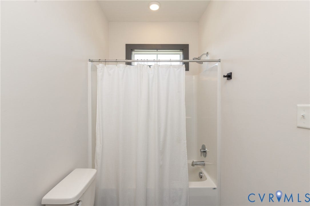 4600 Otter Court, Moseley, VA 23120 Bright bathroom featuring a tub/shower combination with chrome fixtures, a shower curtain rod, and a window with dark trim