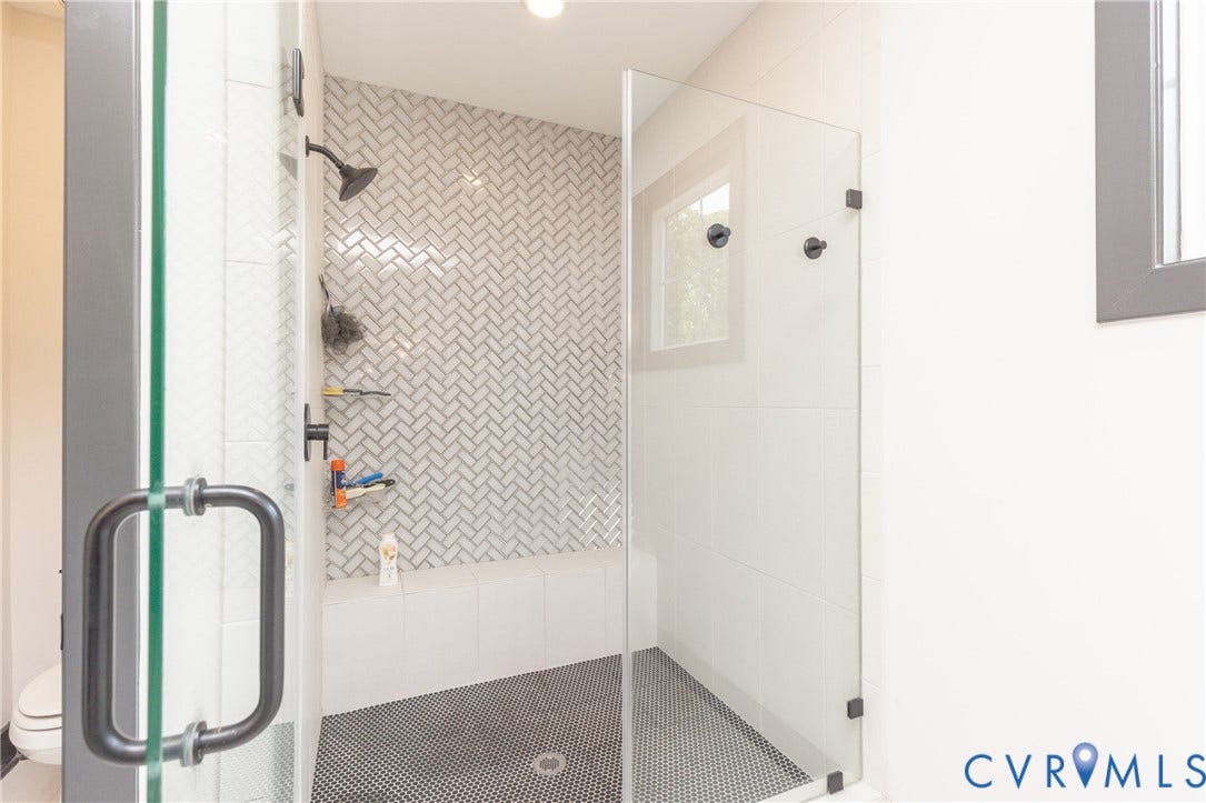 4600 Otter Court, Moseley, VA 23120 Contemporary shower enclosure featuring a glass door with matte black hardware, herringbone-patterned tile, a built-in bench, and black penny tile flooring