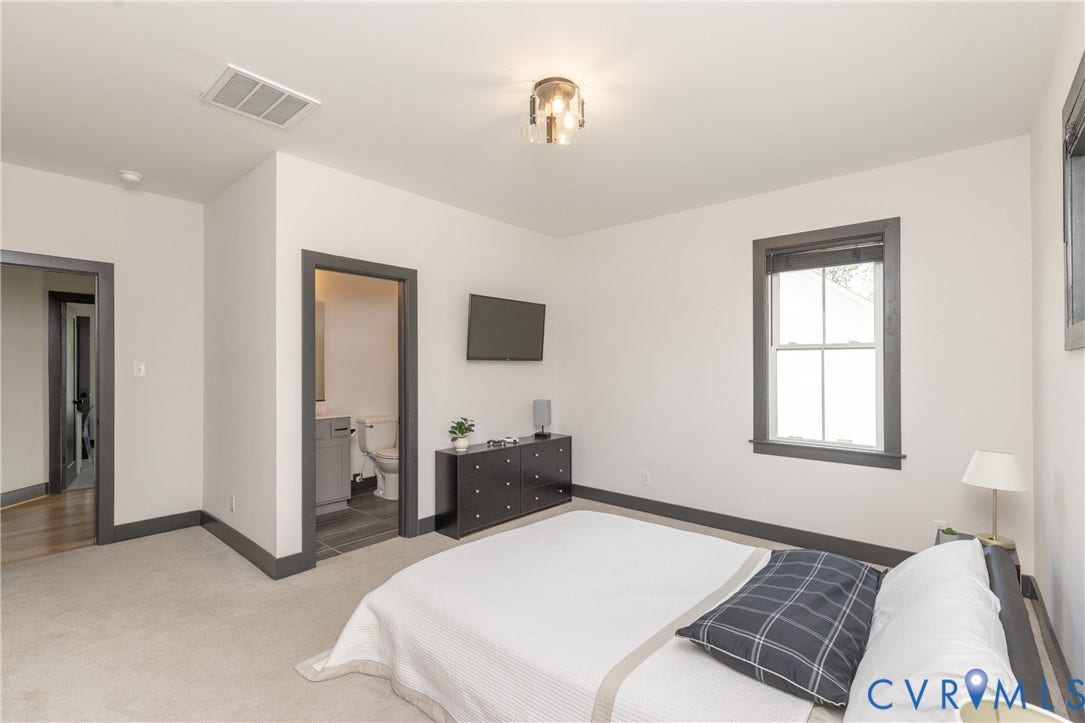 4600 Otter Court, Moseley, VA 23120 Bedroom featuring a double-hung window with dark trim, light neutral carpeting, a ceiling-mounted light fixture, and an entrance to a bathroom with tile flooring and a vanity